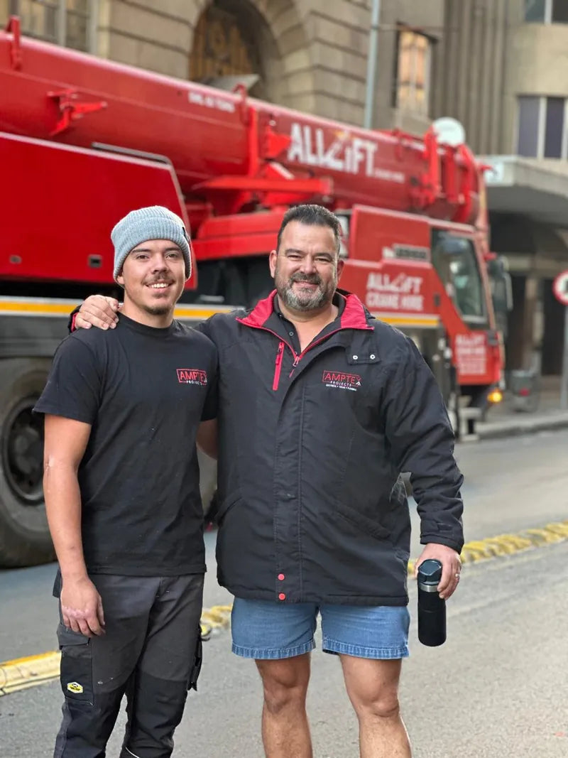 Two Amptex team members standing in a city street in front of a mobile crane