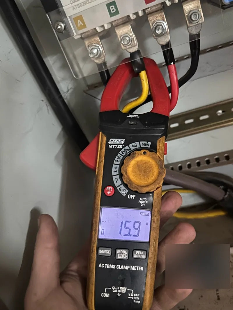 A clamp meter reading 15.9 A on a cable at a three-phase meter