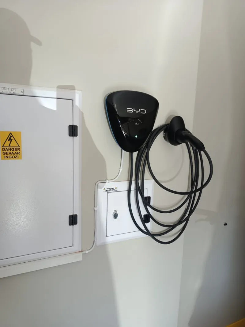 A wall-mounted EV charger with its cable coiled beside a distribution board