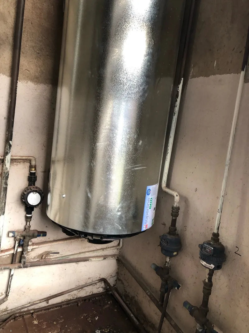 A galvanised geyser with valves and water meters on the pipework below