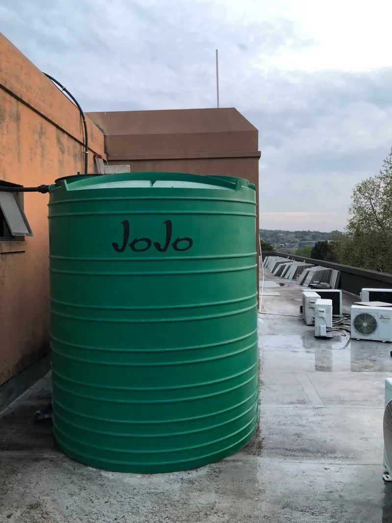 A green JoJo water tank installed on a flat commercial rooftop