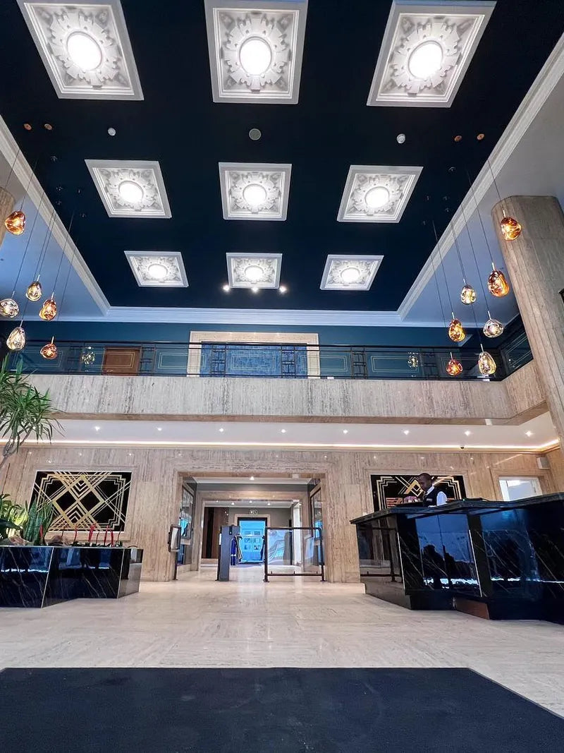 A renovated double-volume lobby with a lit coffered ceiling, planters and a reception desk