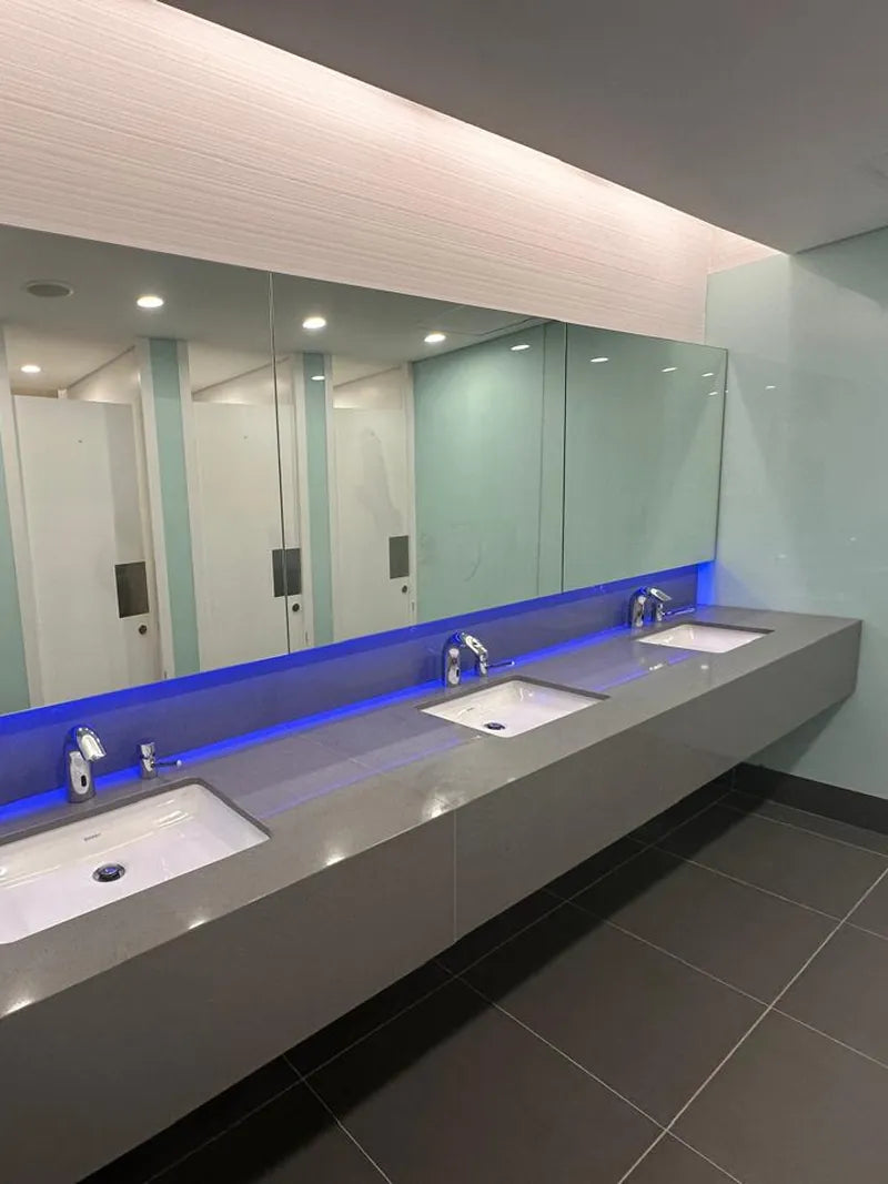 A commercial washroom vanity with sensor taps, basins and blue LED lighting