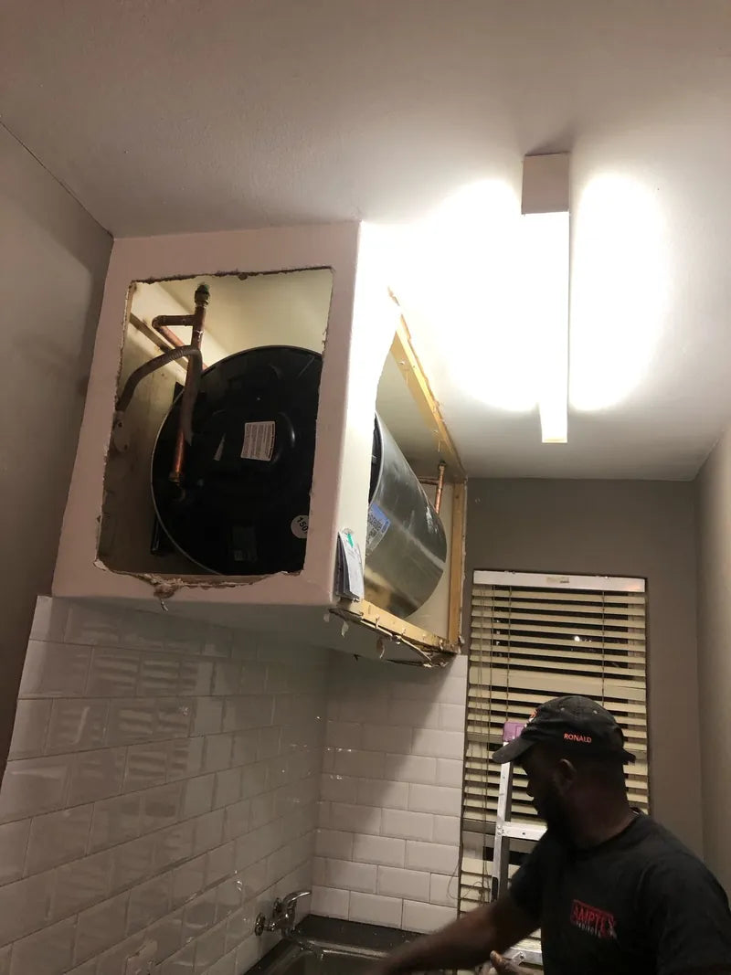 A technician working below a geyser mounted in a bathroom wall cupboard