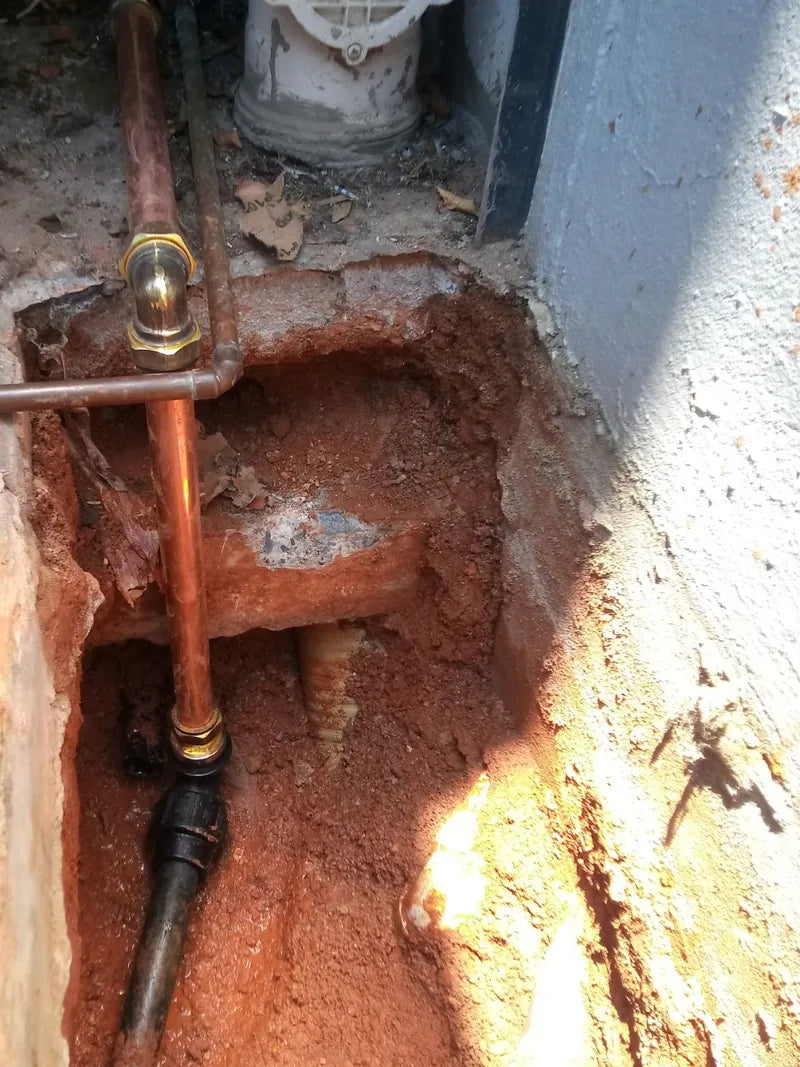 A repaired copper water pipe with a brass fitting in a trench dug beside a wall