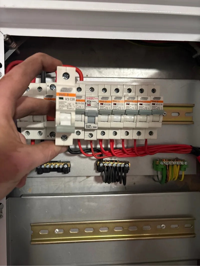 A hand fitting a circuit breaker onto the rail of a distribution board