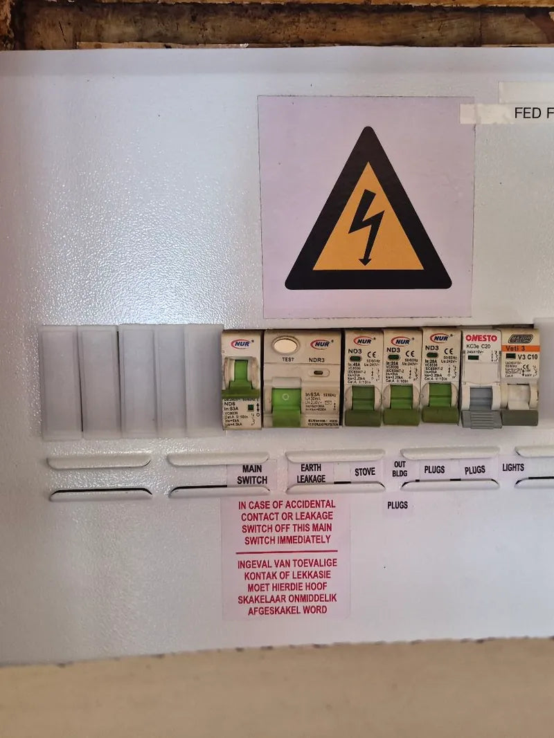A house distribution board with labelled breakers, an electrical hazard sign and a bilingual safety notice