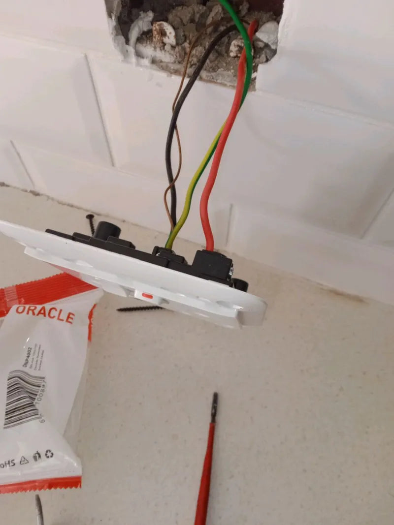 A wall socket pulled out of its box with the wires exposed and a screwdriver below