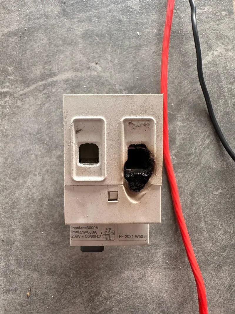A burnt-out plug socket with scorch damage lying on a concrete floor