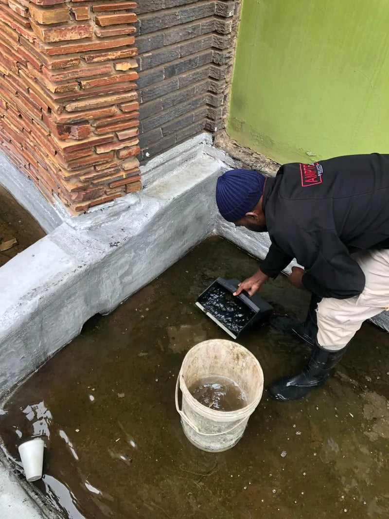 A technician bailing water from a flooded courtyard into a bucket
