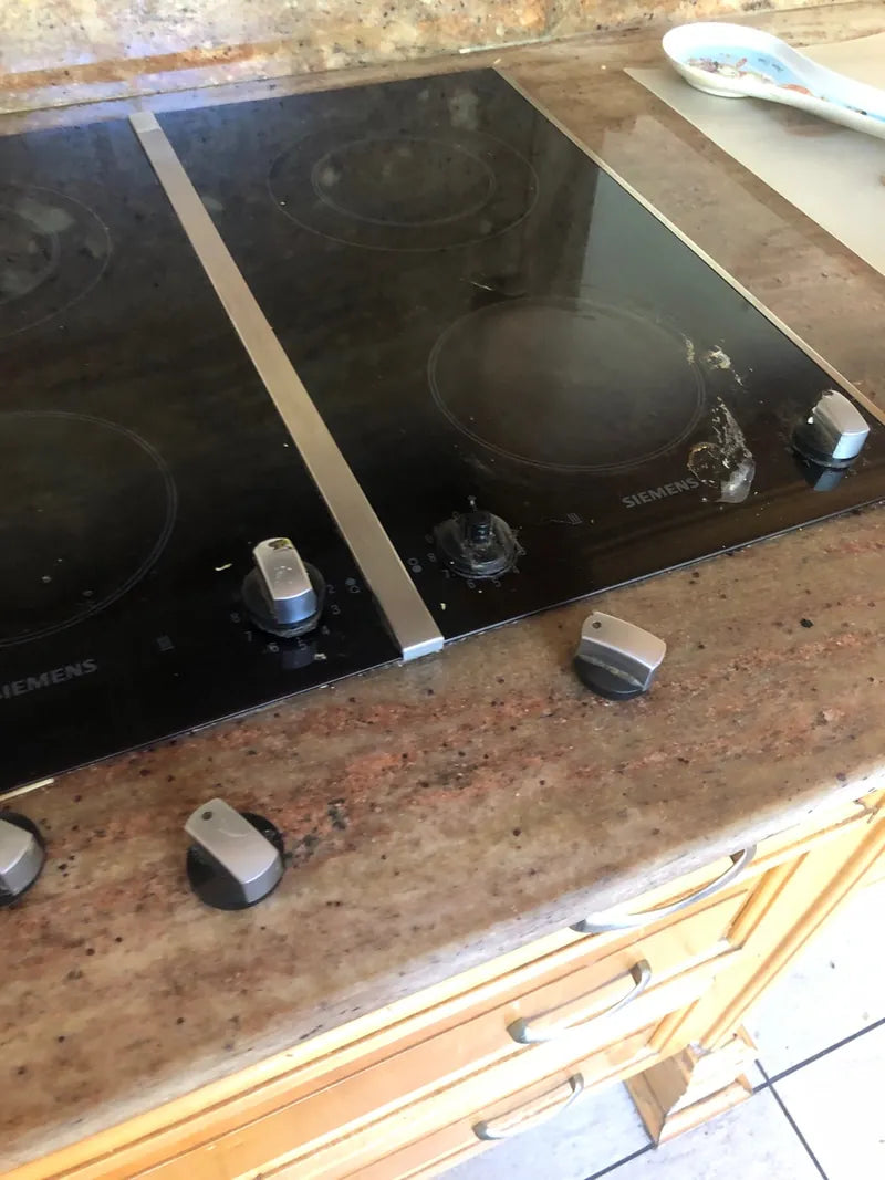 A ceramic glass hob with control knobs set into a granite kitchen counter