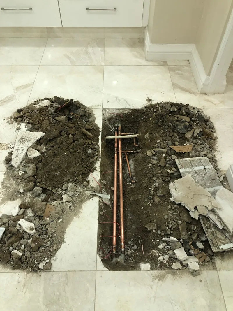 A tiled floor opened up to expose copper water pipes during a leak repair